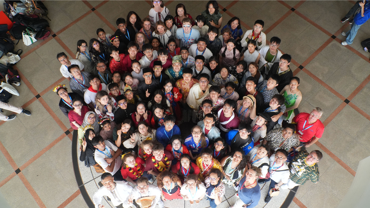An overhead, top-down view of summit participants standing close together in a circle on a tiled floor, looking up at the camera.