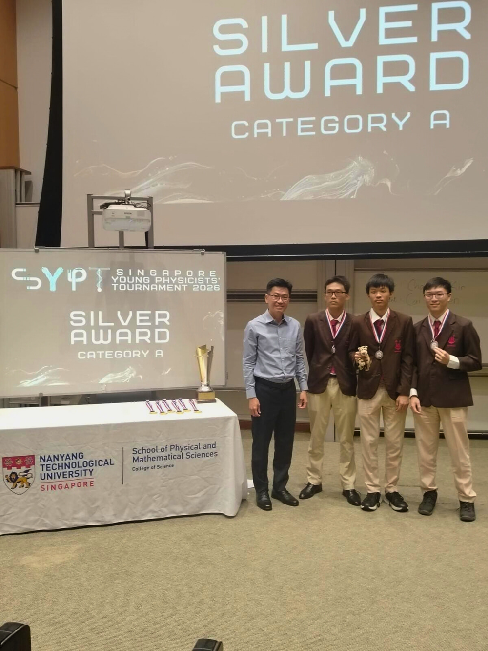 Four people stand beside a table with a trophy at the Singapore Young Physicists Tournament 2026 Silver Award Category A.