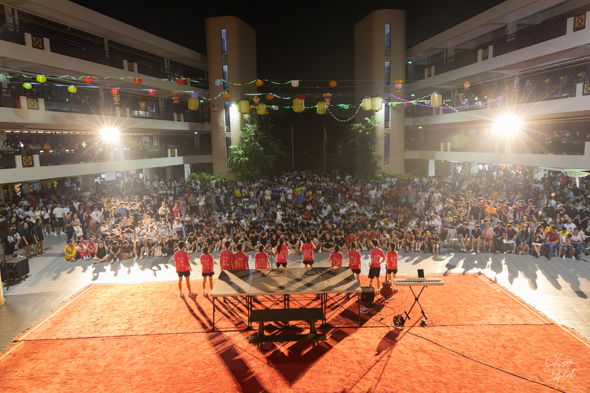 Student councillors on stage facing a large crowd of students gathered in the central plaza during the Hwa Chong Institution Mid-Autumn Festival celebration.