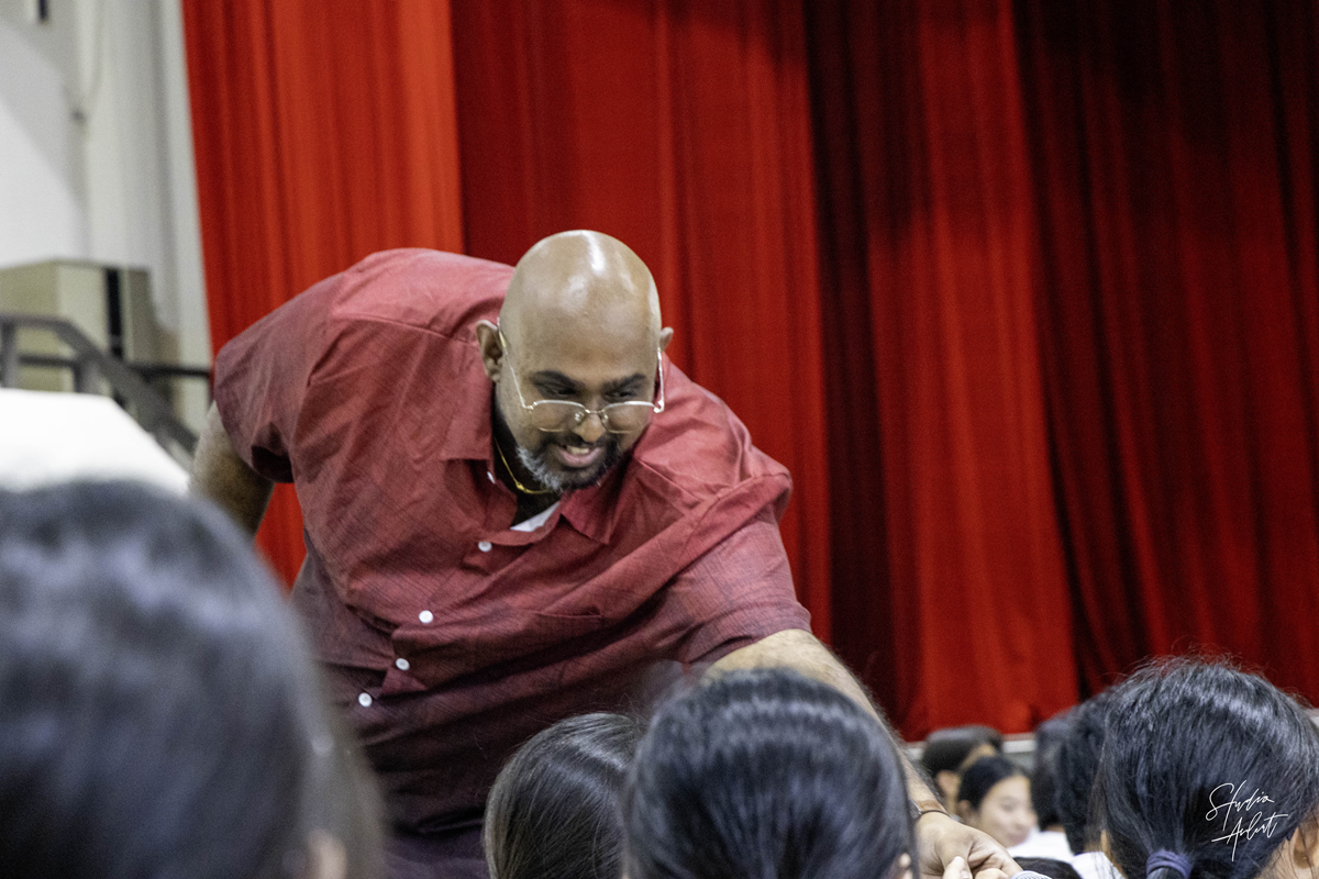 Guest speaker Niranjan Pandian leaning down from the stage to interact closely with C2 students.