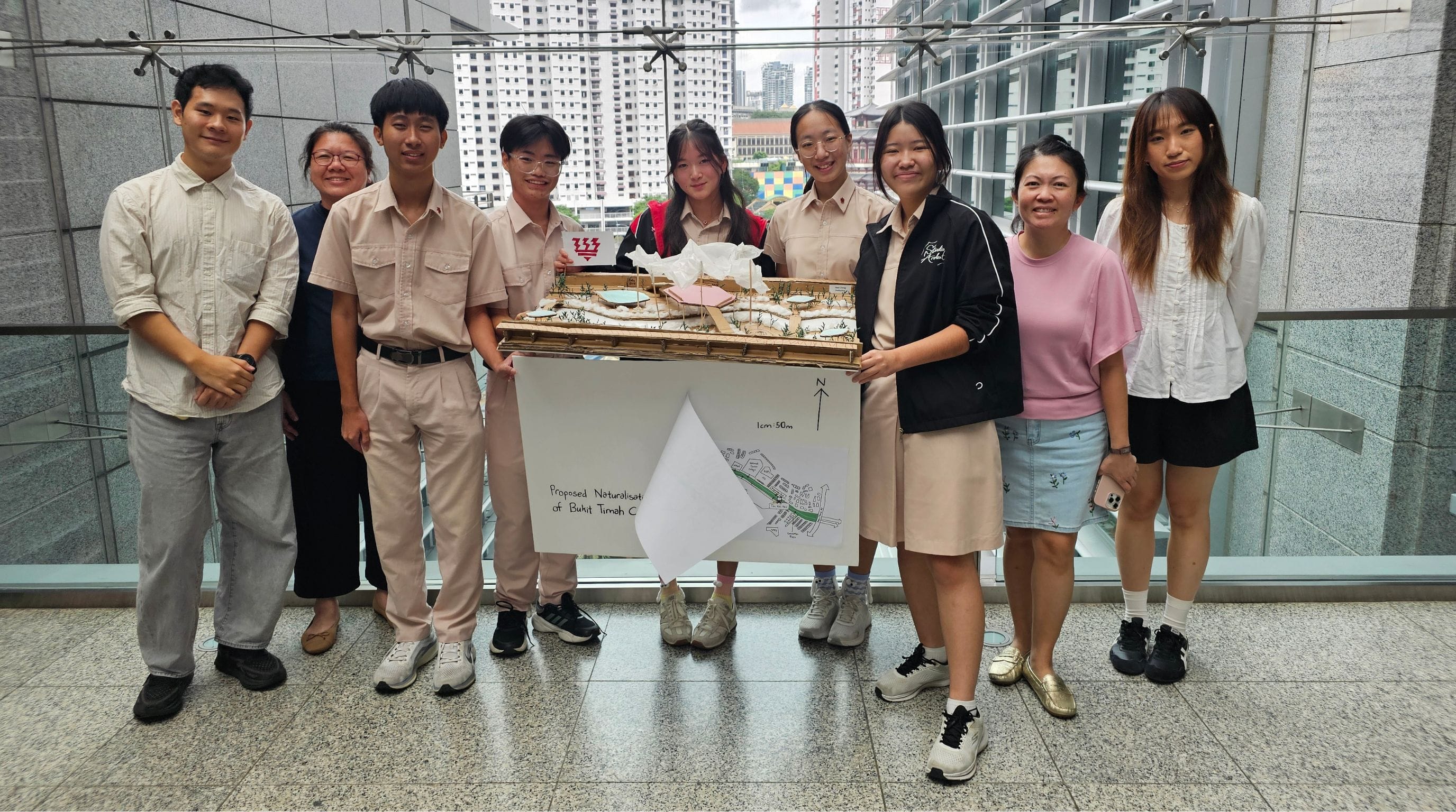 Eight students pose holding a scale architectural model and a map labeled Proposed Naturalisation of Bukit Timah Canal.