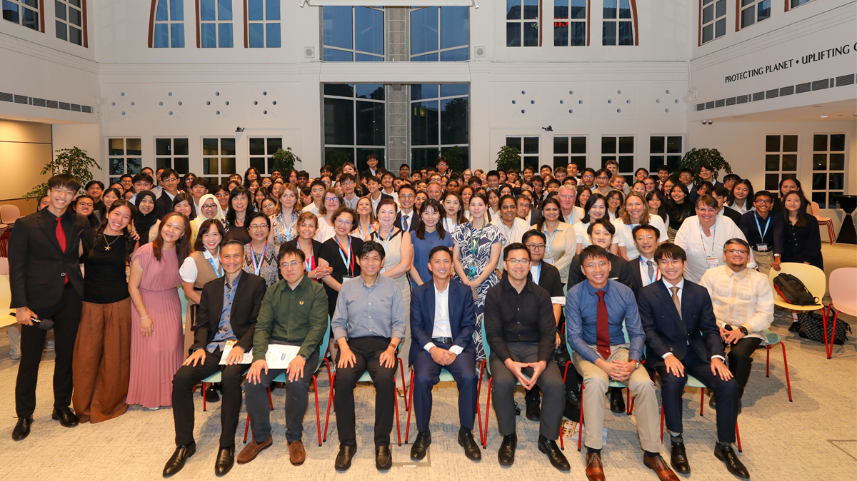 A large group photo of HC-APYLS student delegates and staff smiling and posing together in an indoor school hall.