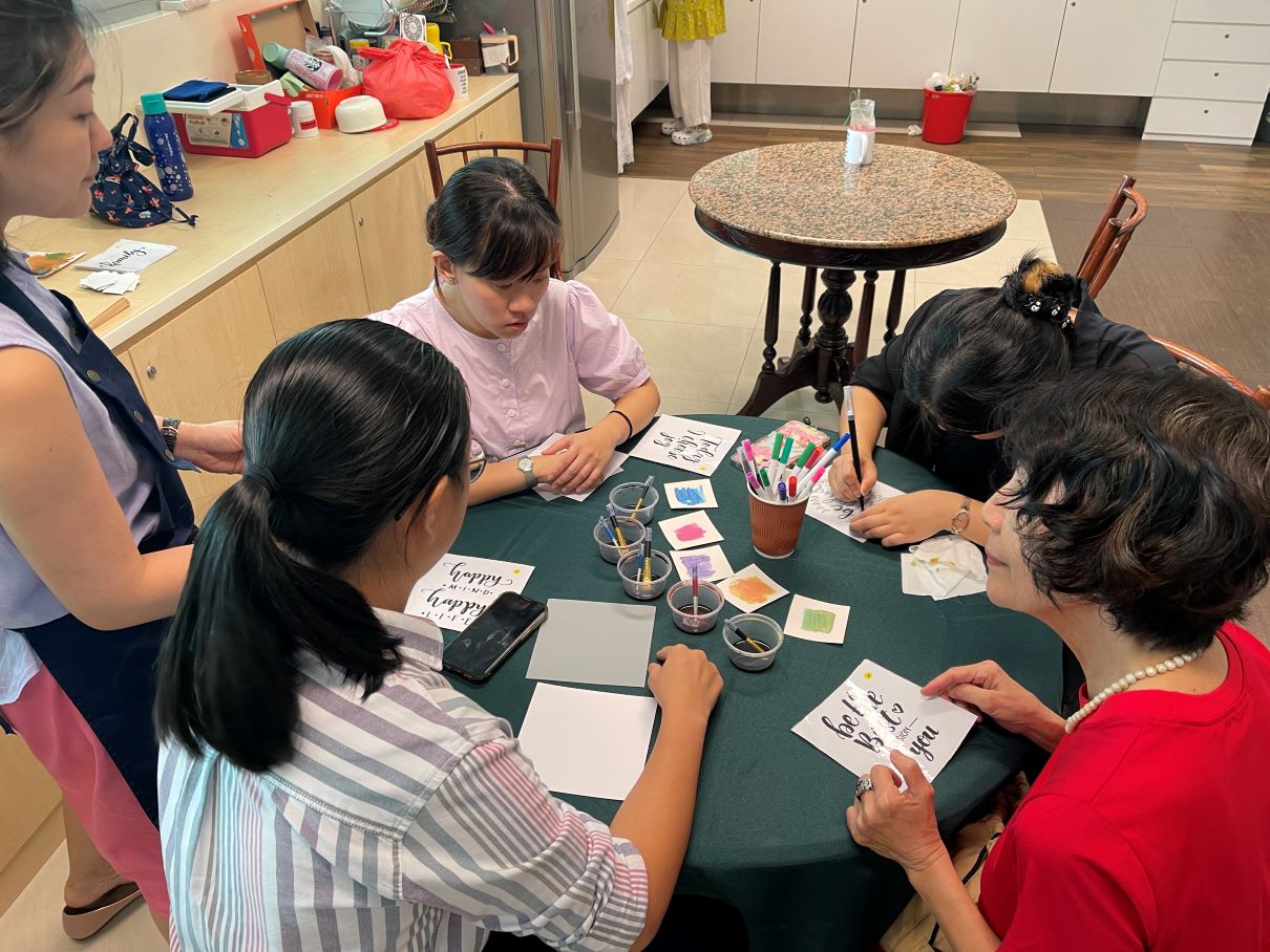 A small group sits around a table creating hand-lettered cards and watercolor artwork during a craft workshop