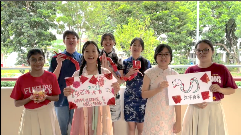 Seven students holding Chinese New Year signs with snake drawings and the text Happy Chinese New Year outdoors.
