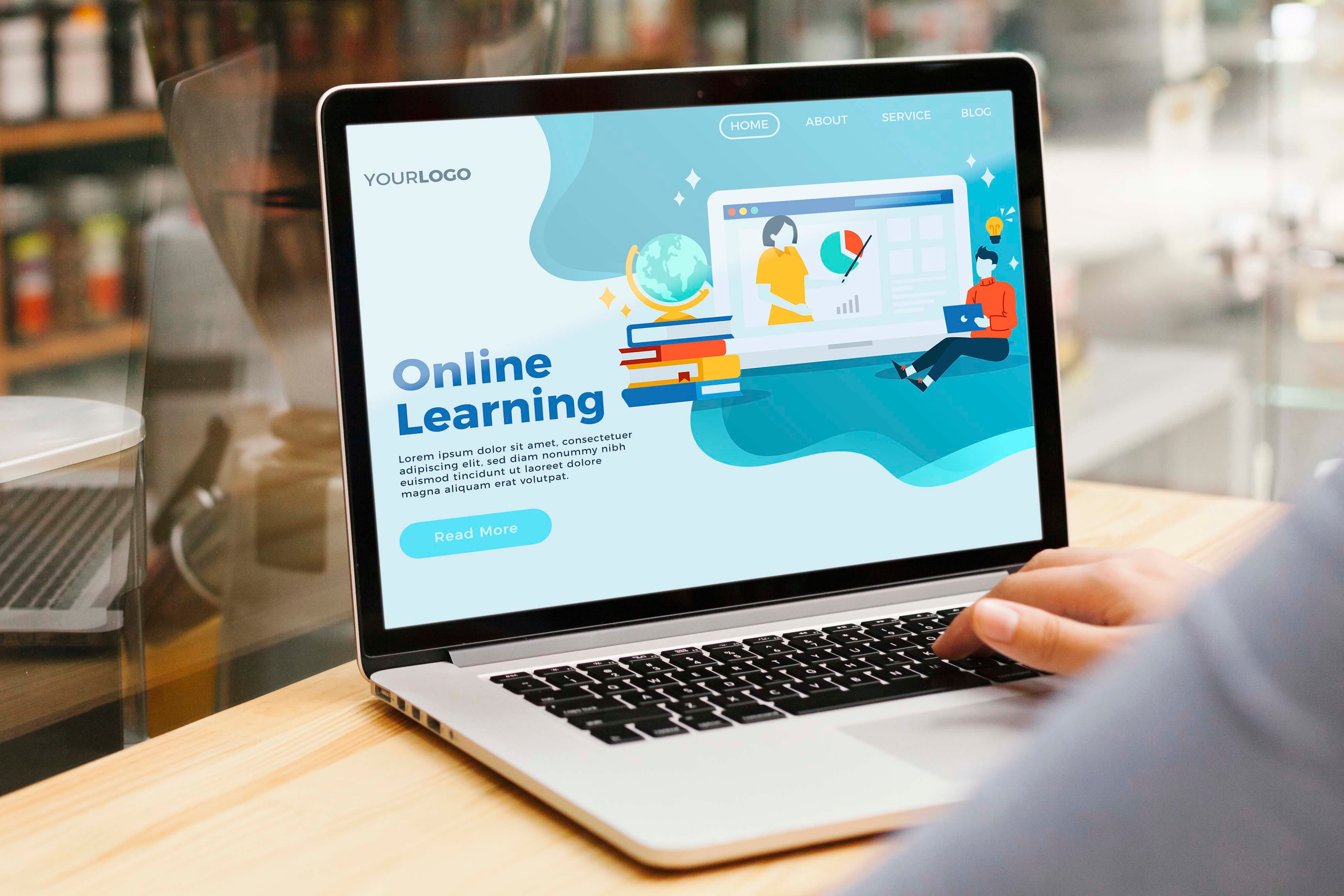 A hand uses a laptop displaying a blue Online Learning website with cartoon students, books, and a globe.