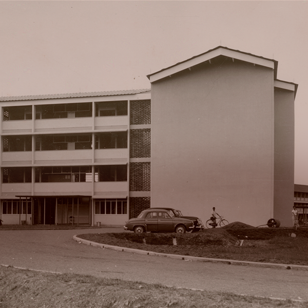 Vintage sepia photo of a four-story building with a parked car and bicycle near the entrance.