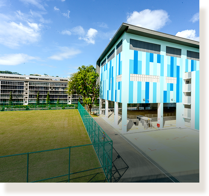 A multi-story blue and white patterned school building beside a green sports field under a blue sky.
