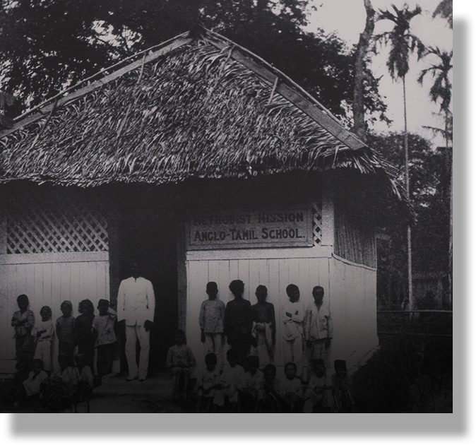 Black and white photo of people standing outside the Methodist Mission Anglo-Tamil School, a thatched-roof building.