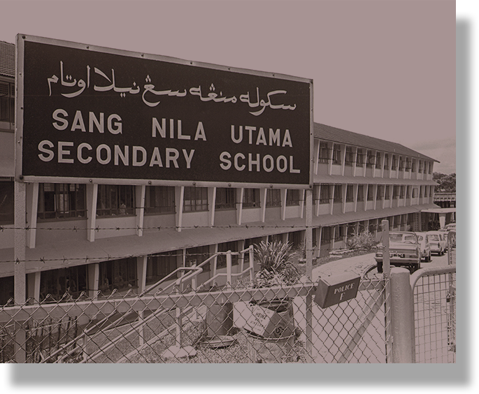 Black and white photo of Sang Nila Utama Secondary School building with a large bilingual sign in English and Jawi.