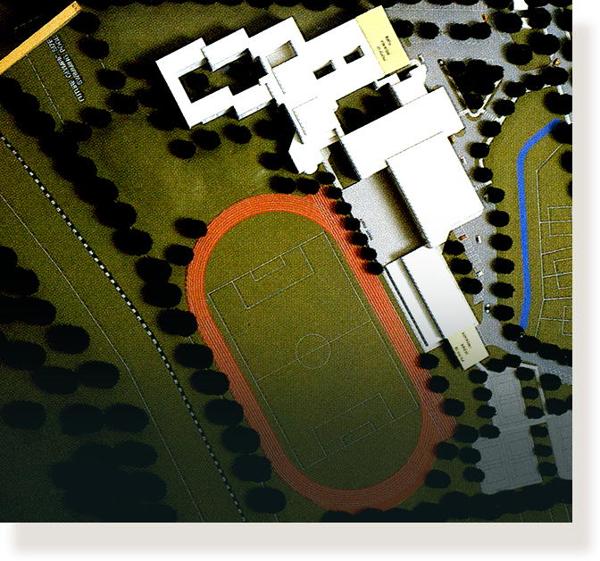 Aerial architectural scale model showing a school campus with a red running track, soccer field, and white building blocks.