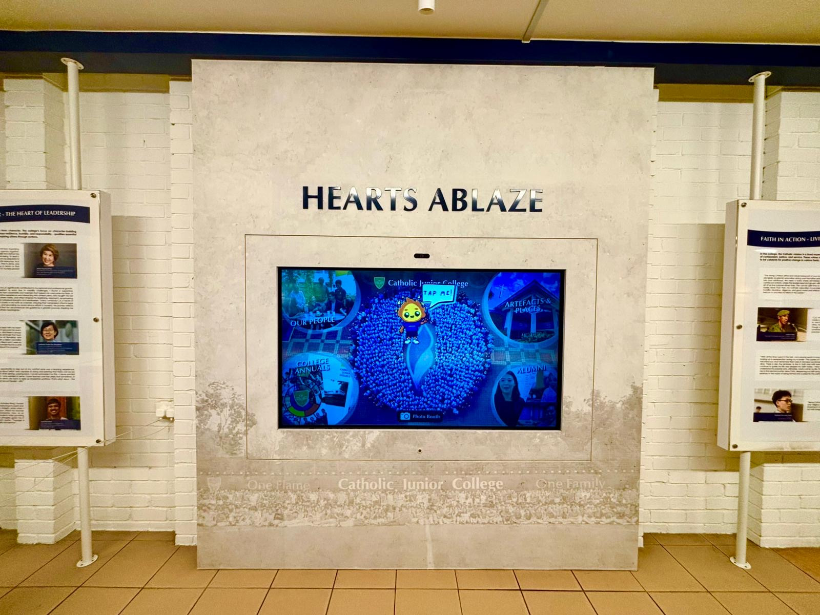An interactive touchscreen kiosk display at Catholic Junior College, headed by the title 'Hearts Ablaze' in bold lettering. 