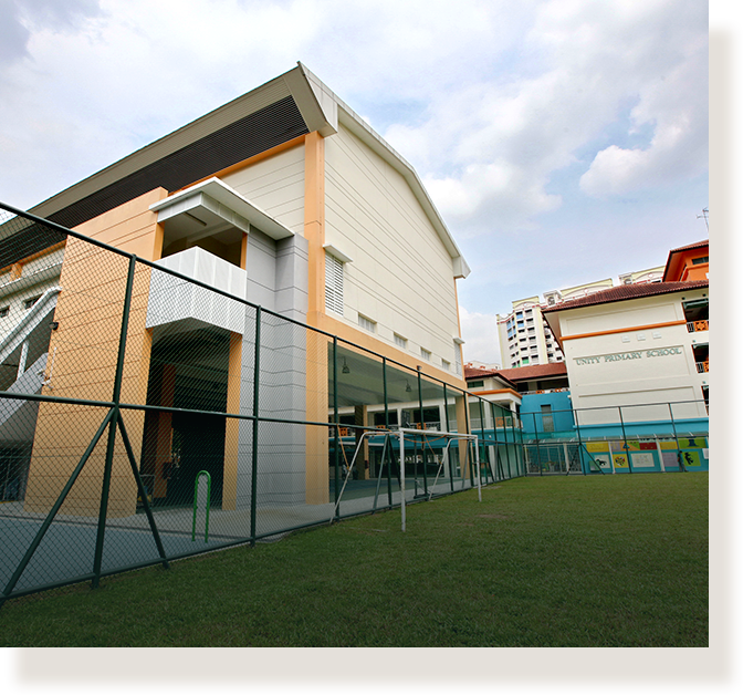 Exterior of Unity Primary School with a fenced grass field, multi-story buildings, and a partly cloudy sky.