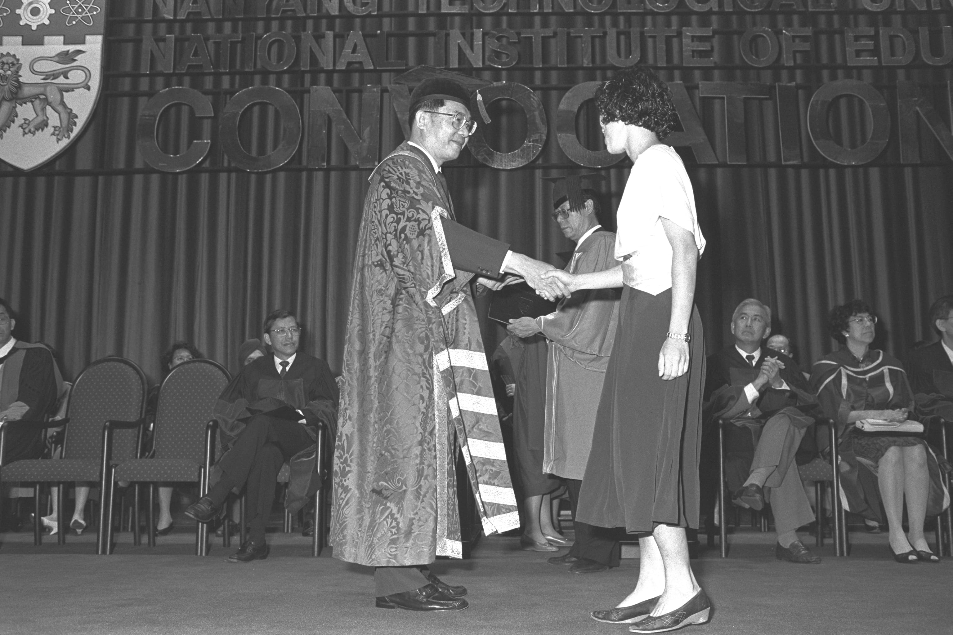 A robed official shakes hands with a graduate on stage at Nanyang Technological University's convocation ceremony.