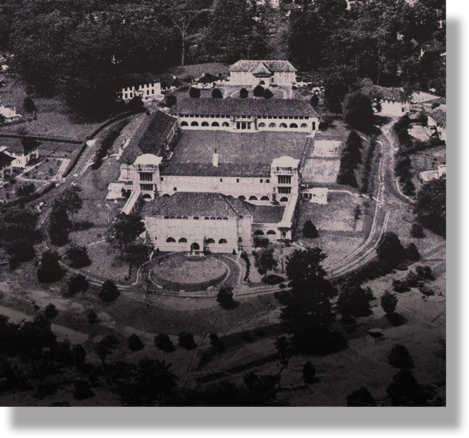 Black and white aerial view of a large historic estate with arched architecture, courtyards, and surrounding trees.