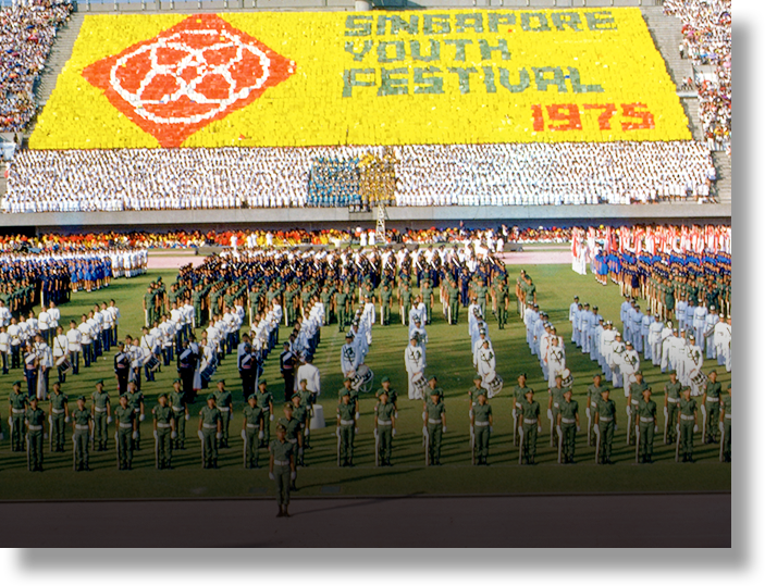 Large stadium ceremony for Singapore Youth Festival 1975, with rows of uniformed participants on a field and a colorful card display.