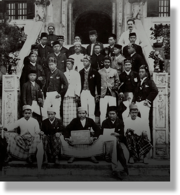 Black and white historical photo of a large group of men in formal and traditional attire posed on building steps.