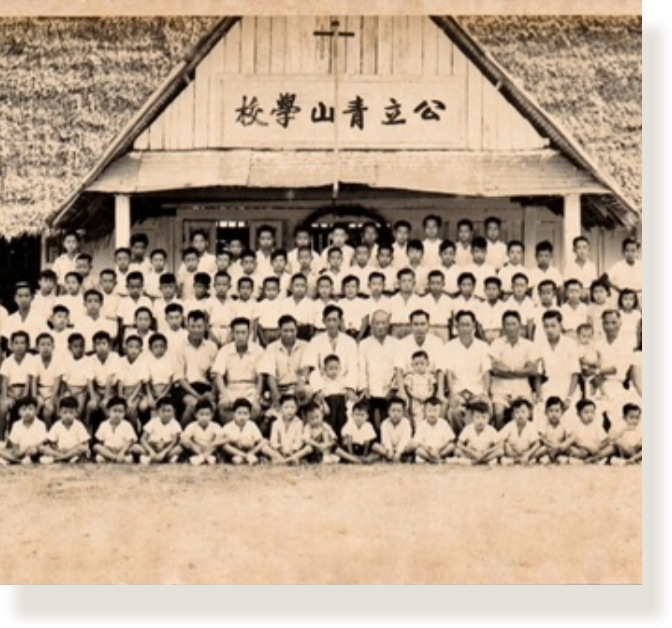 Old sepia group photo of many children and adults posing in front of a building with Chinese characters above.