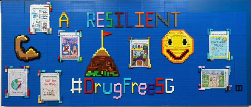 Blue LEGO board displaying "A Resilient" and "#DrugFreeSG" with pixel art icons and anti-drug poster displays.
