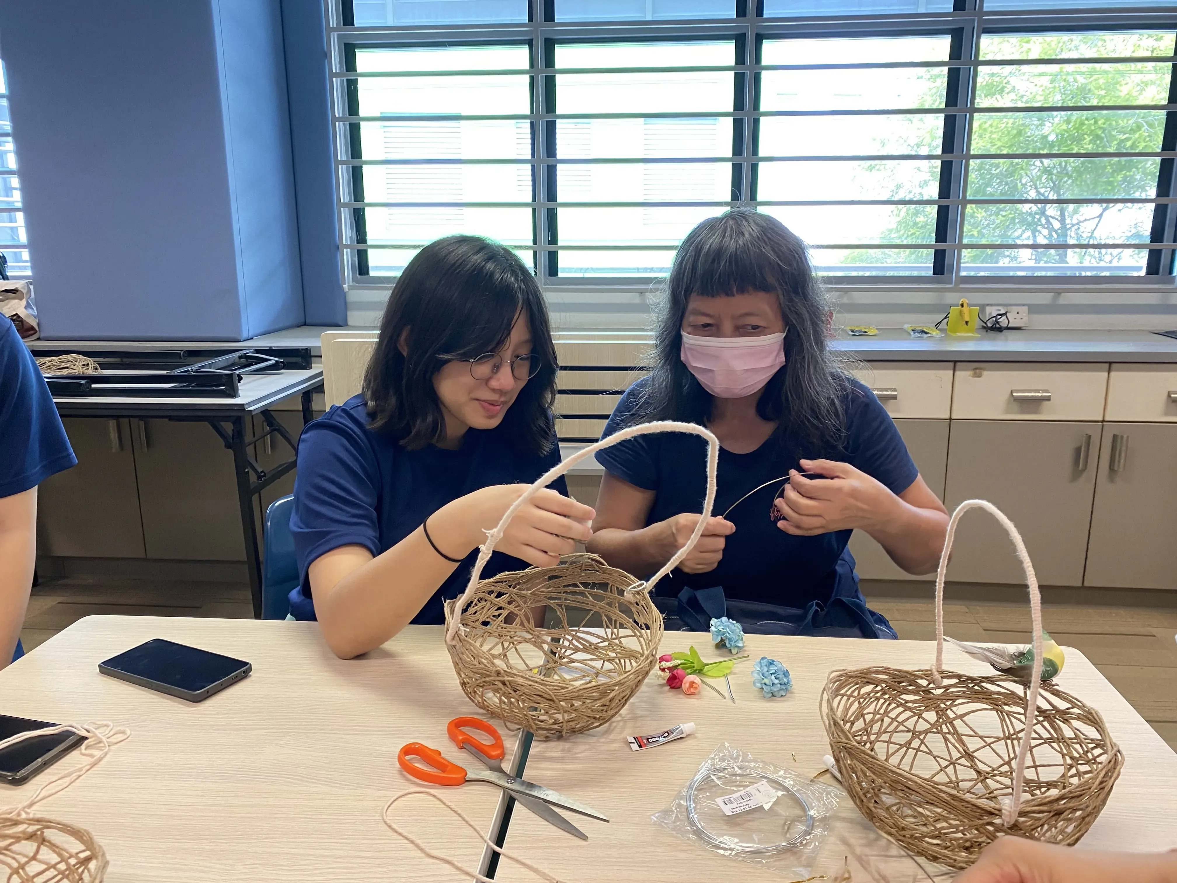 A student from Ang Mo Kio Secondary School guided a senior in crafting plant hangers using twine and techniques like weaving and knotting..