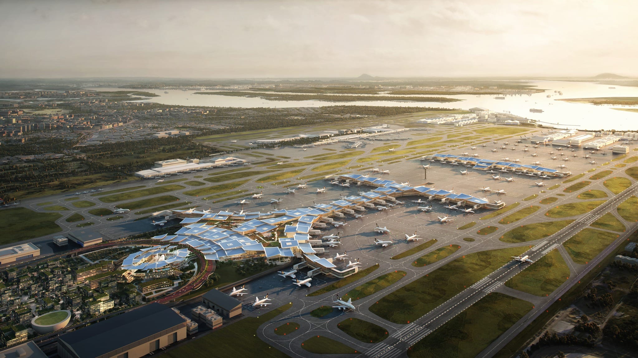 Aerial view of a large airport with blue-roofed terminals, multiple planes on tarmac, runways, and a city and water beyond.