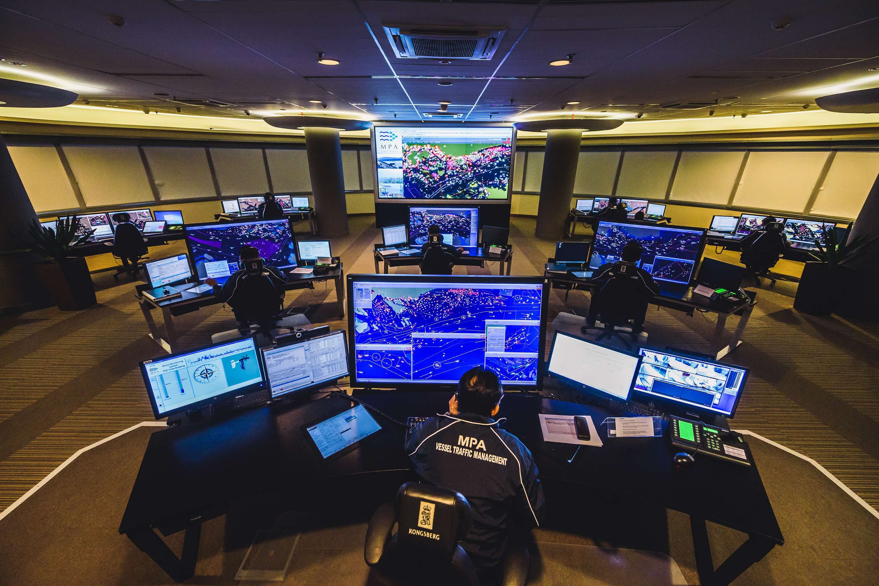 MPA Vessel Traffic Management control room with operators at multi-monitor workstations displaying nautical charts and ship tracking data.