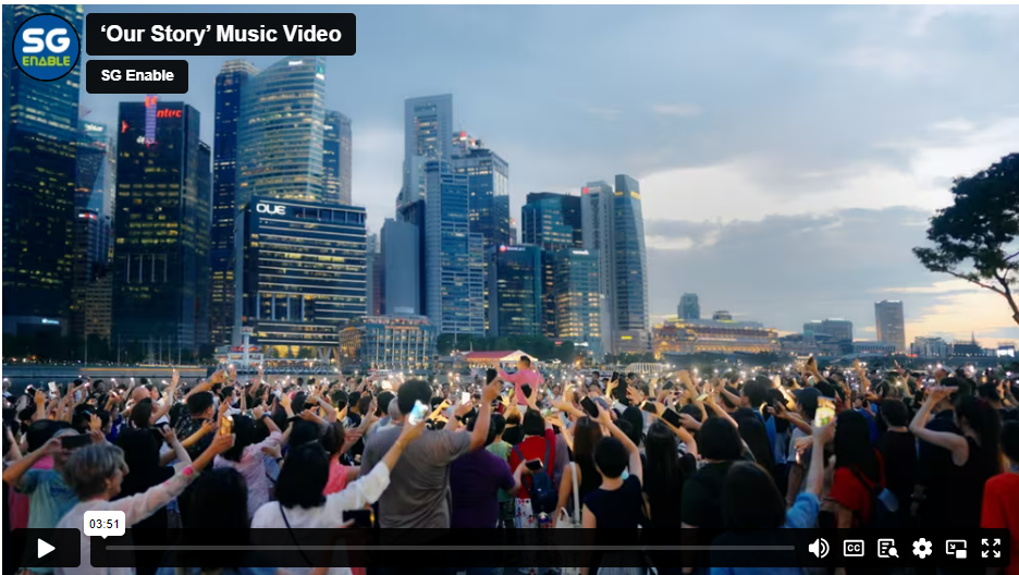 A large crowd raises hands and phones in front of Singapore's illuminated skyline at dusk in a music video thumbnail.