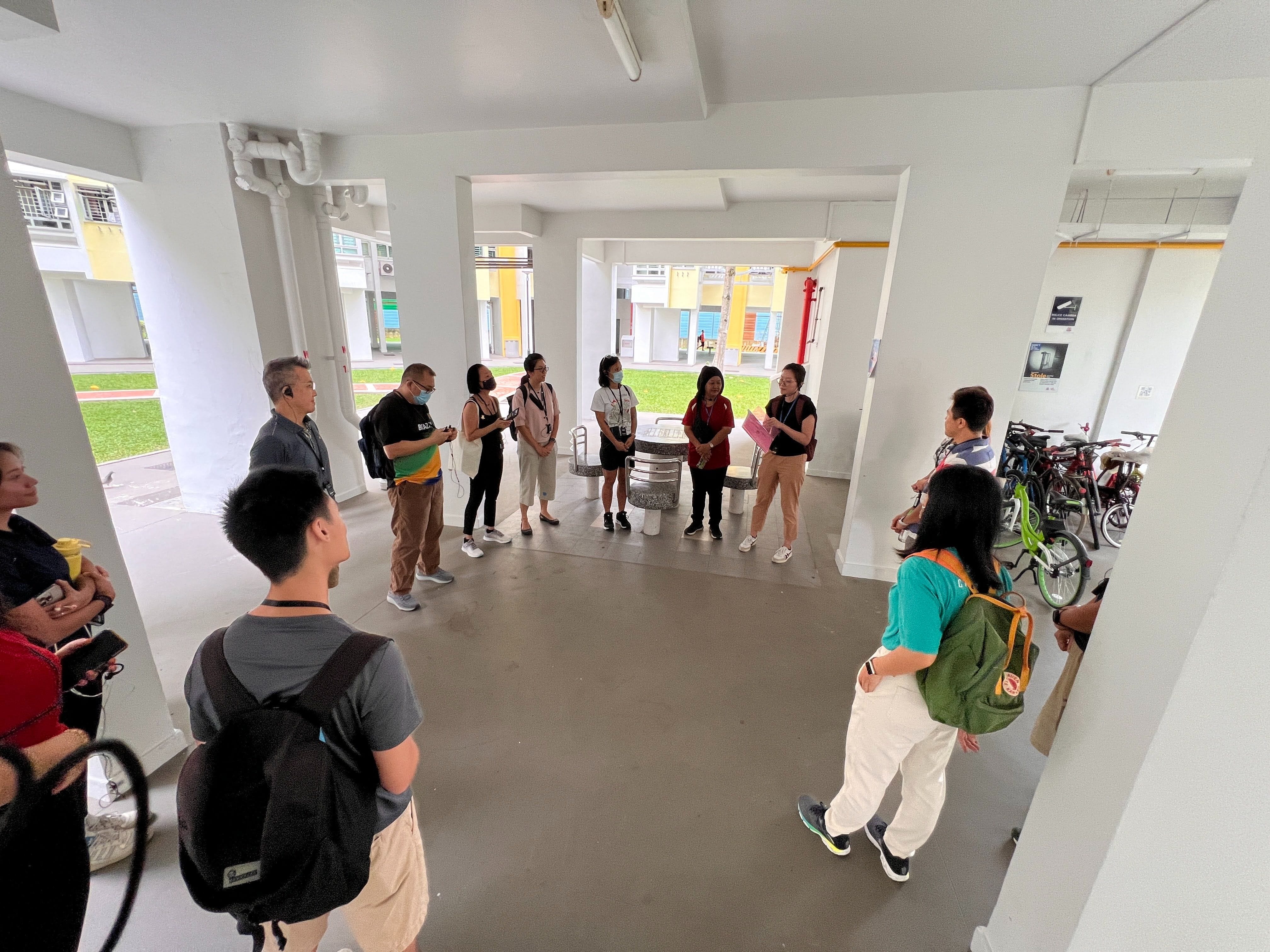 A group of about ten people stand in a circle in an open covered corridor of a residential block.