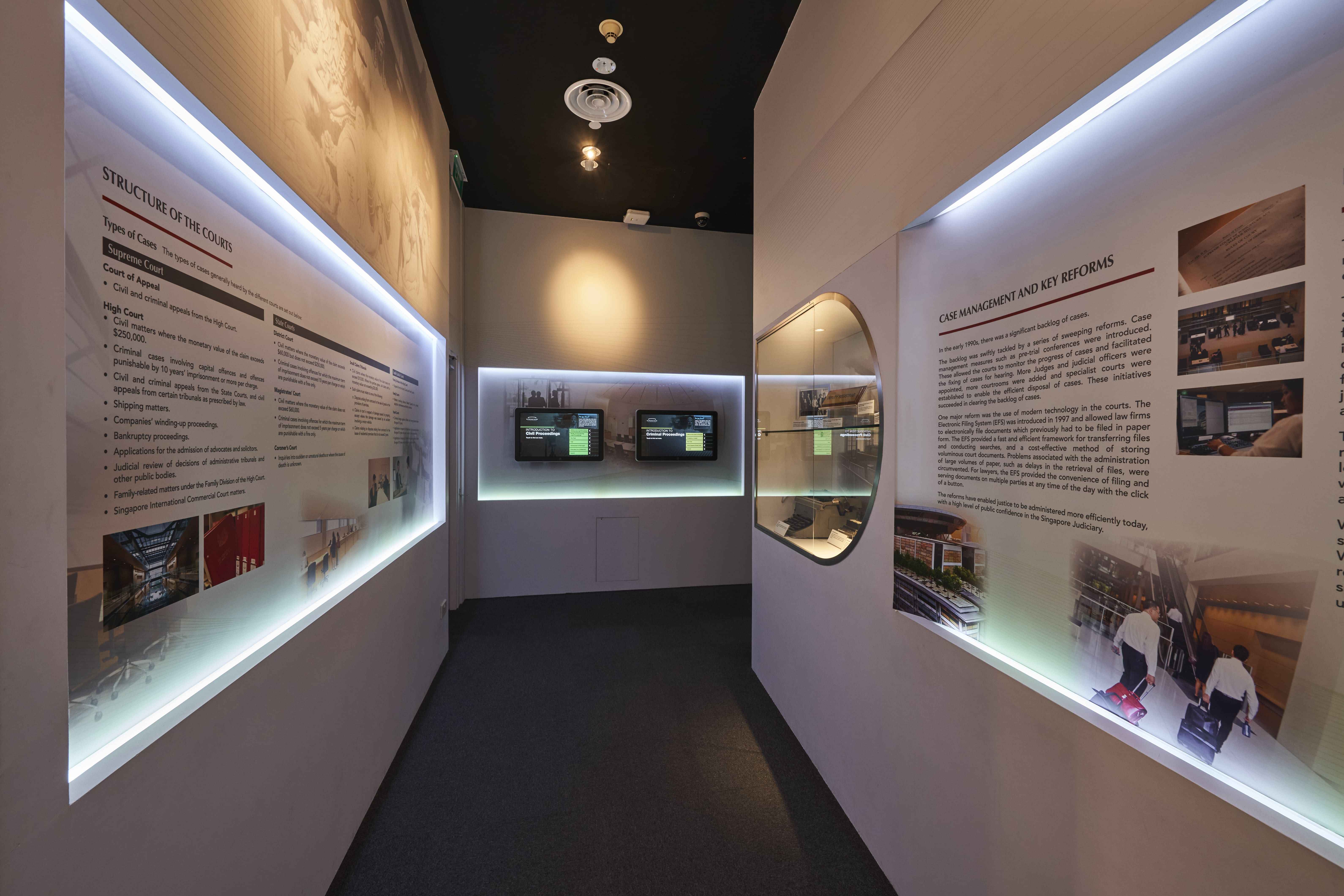 A museum corridor with lit display panels about court structure and key reforms, two screens, and glass display cases.