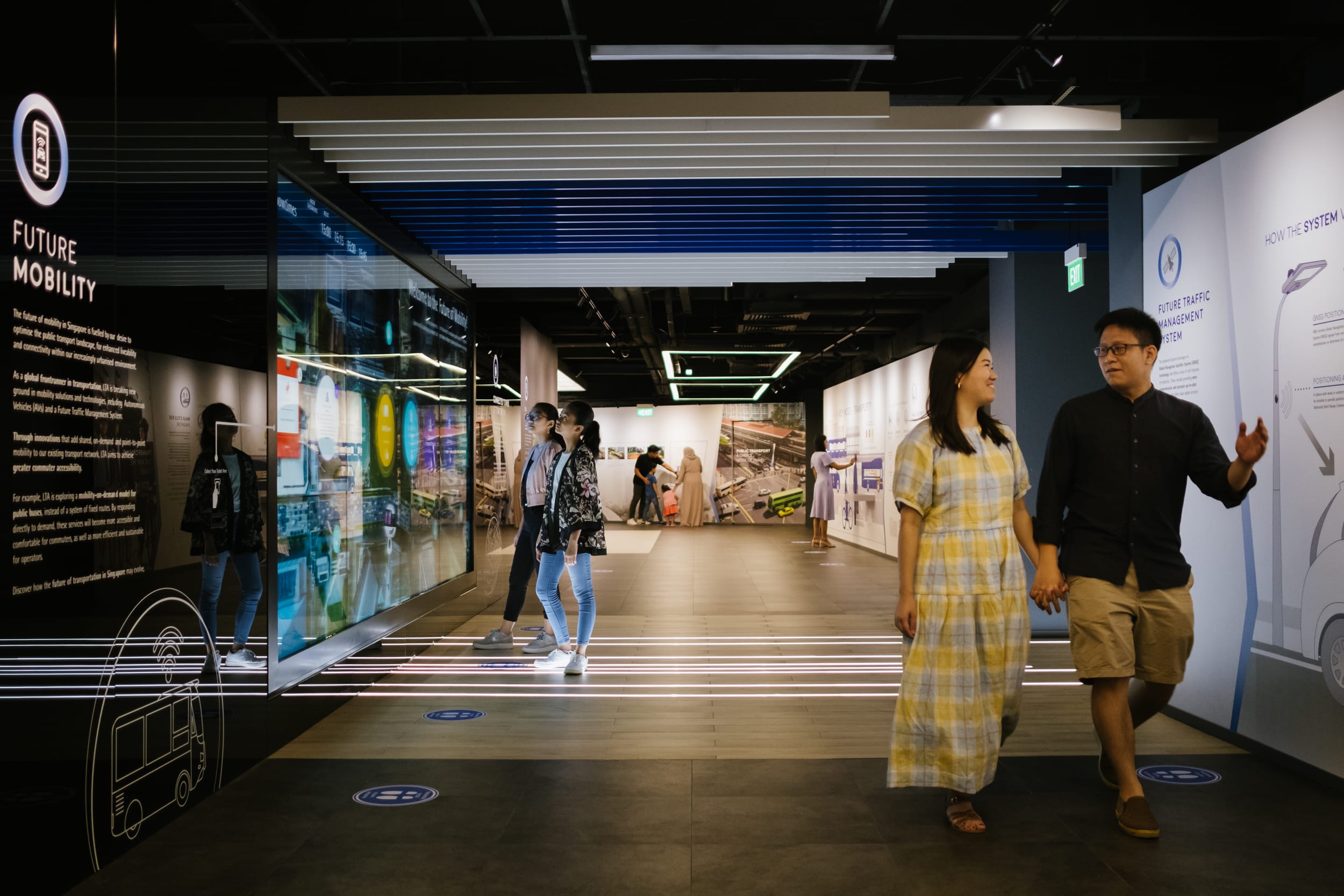 Visitors walk through a Future Mobility exhibition hall with lit displays and informational panels on transportation.
