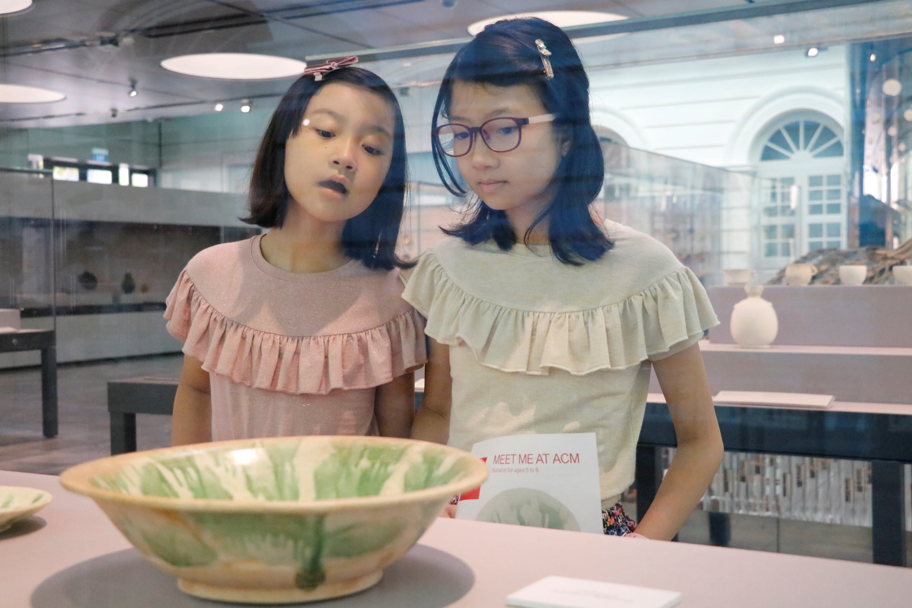 Two young girls look closely at a green and cream ceramic bowl on display at the ACM museum.