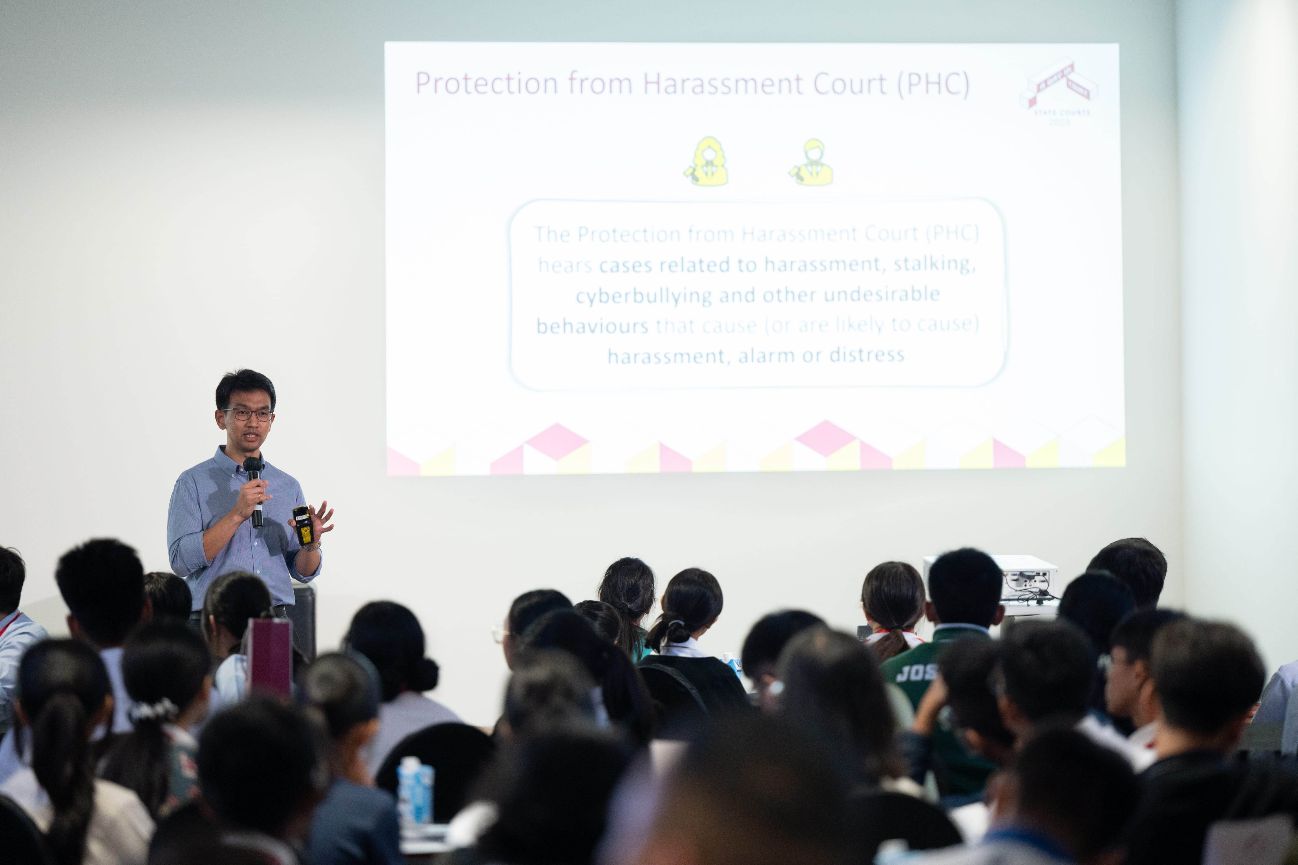A man with a microphone presents a slide about Protection from Harassment Court to a large seated audience.