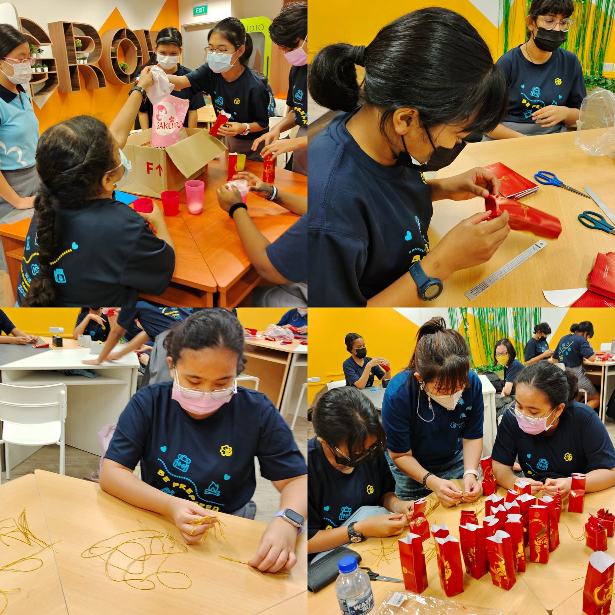 Students in navy shirts and masks craft red decorative bags with gold ribbon in a colorful classroom.
