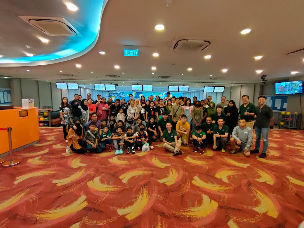 Large group of adults and children posing together inside a bowling alley with red patterned carpet.