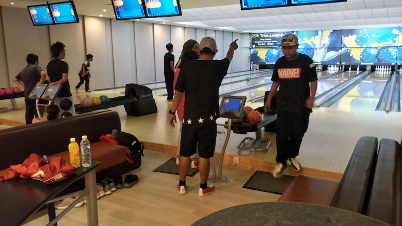 People in a bowling alley with lanes, pins, and colorful bowling balls visible on ball returns.