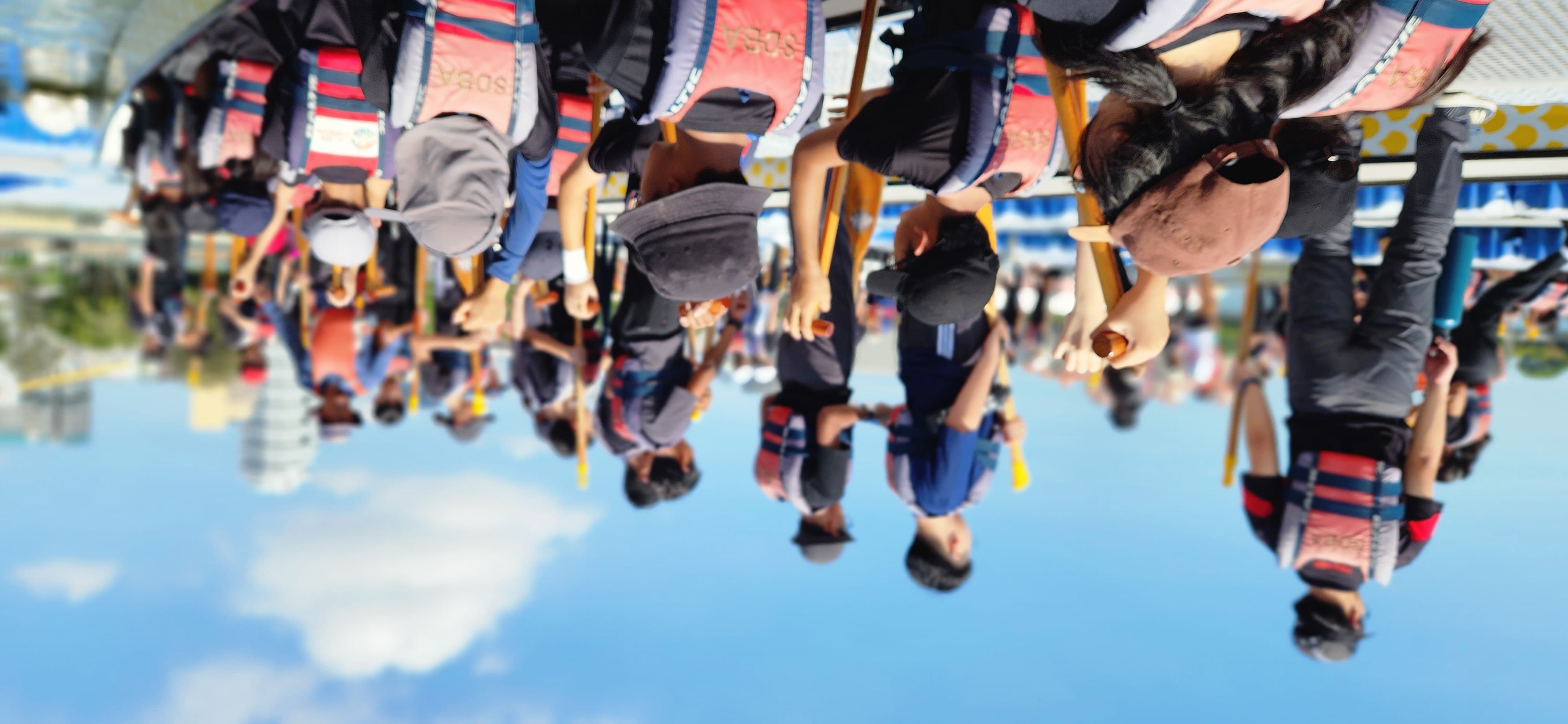 A group of people wearing life vests hold paddles on a dragon boat under a blue sky.