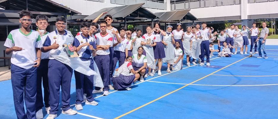 A large group of school students in uniforms posing on a blue outdoor court on a sunny day.
