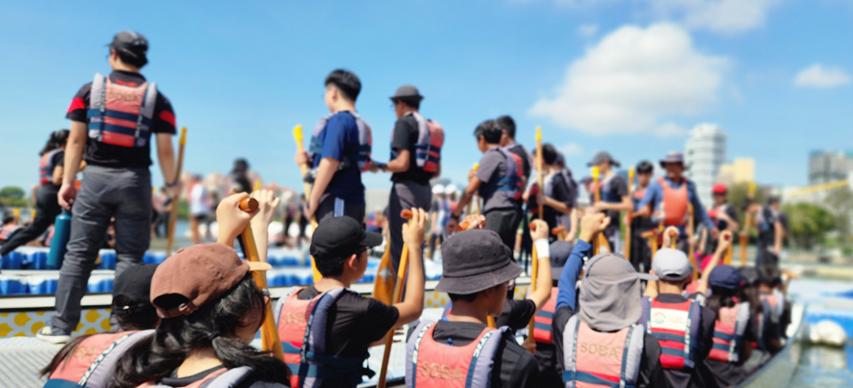 A group of people in life vests holding paddles on dragon boats on a sunny day.