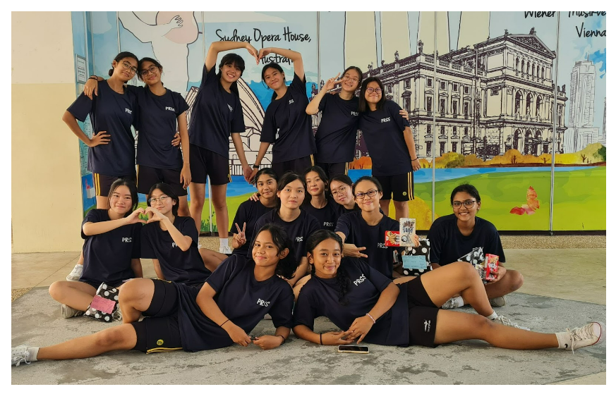 Group of teenage girls in matching navy uniforms posing in front of a colorful mural of the Sydney Opera House.