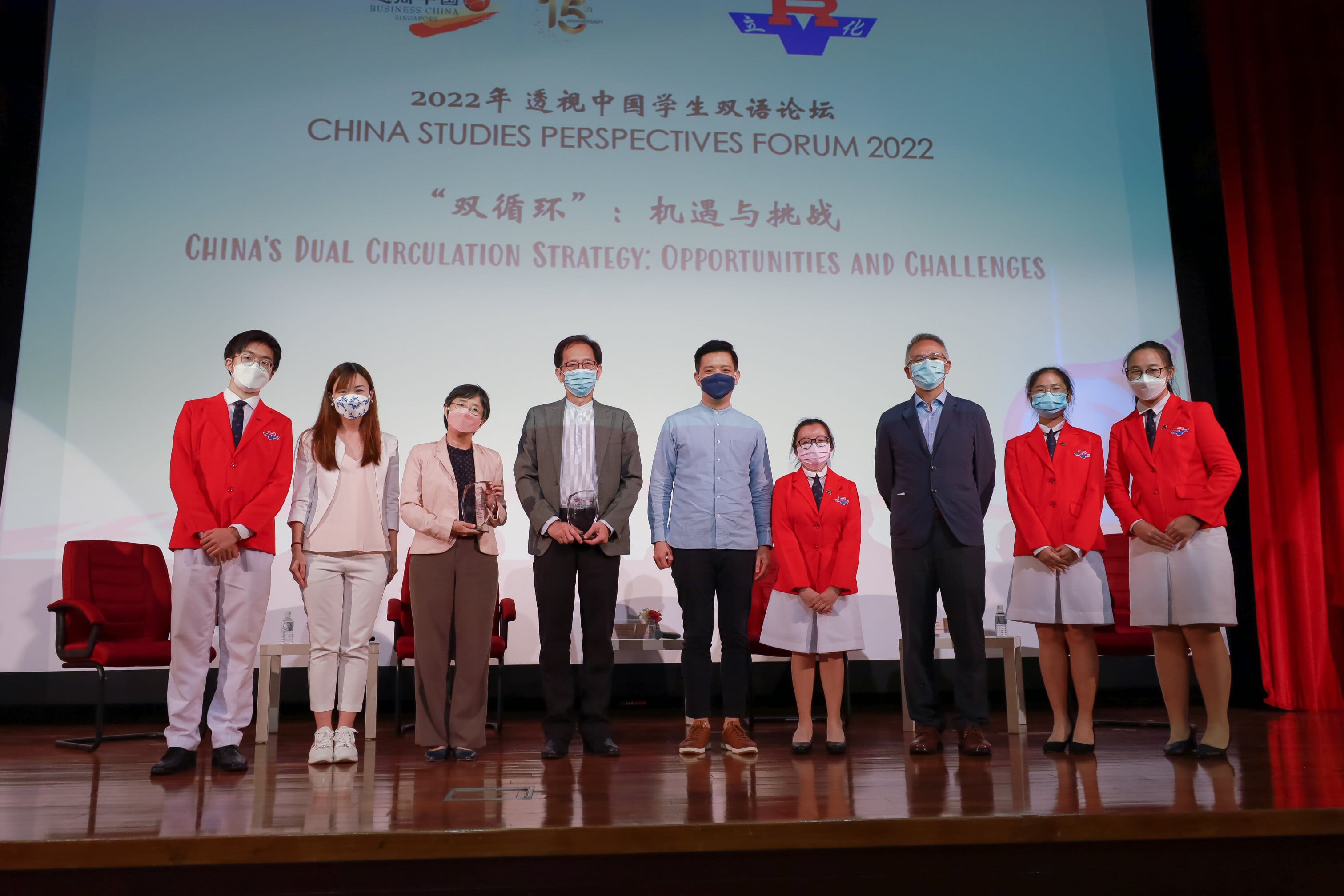 Eight masked people pose on stage at the China Studies Perspectives Forum 2022, some holding crystal awards.