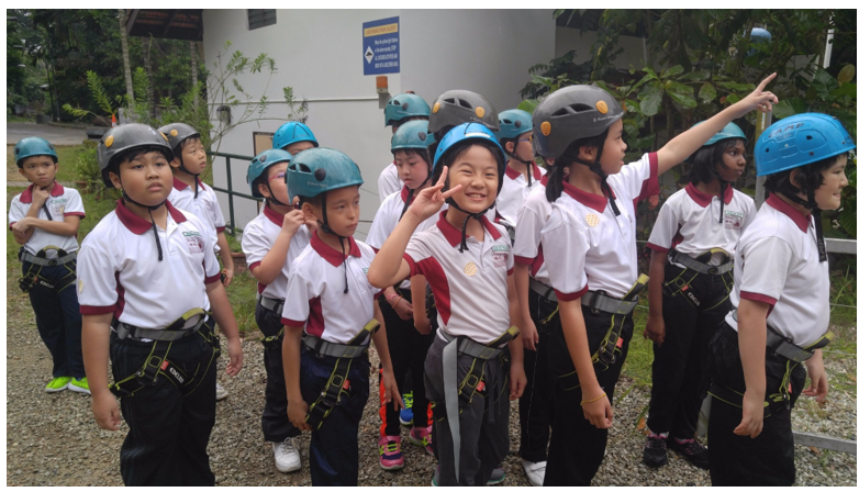 Group of young students in white uniforms wearing blue and gray helmets and harnesses outdoors.
