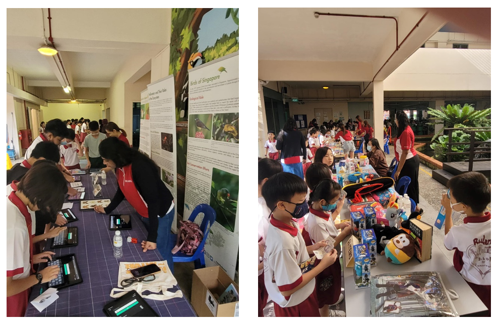 Students in uniforms gather at tables during a school event, with educational posters and toys displayed nearby.