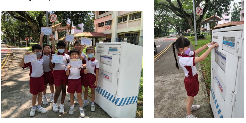 Five masked children in school uniforms hold up drawings near a white post box; one girl posts a letter into it.