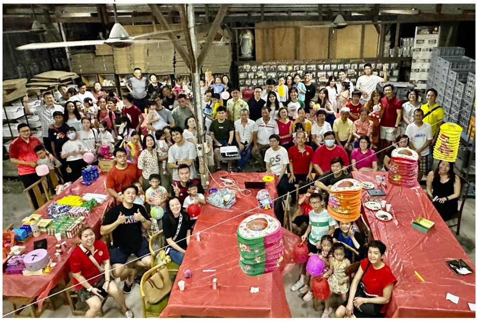 Large group of people gathered indoors around red-covered tables decorated with colorful lanterns for a Mid-Autumn Festival celebration.