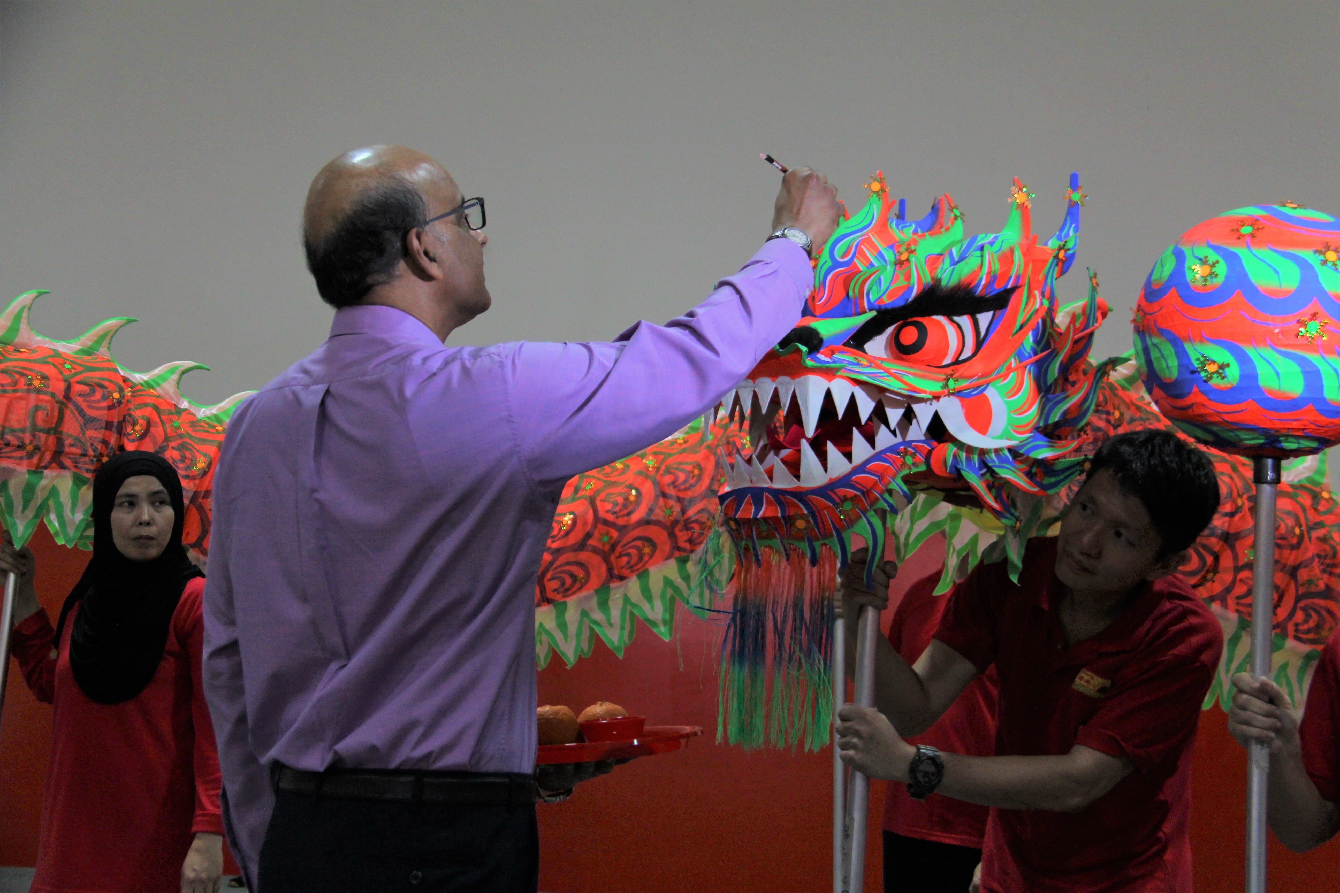 A man in a purple shirt paints the eye of a colorful dragon dance costume held by performers in red.