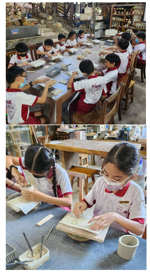 Children in matching uniforms and masks work on clay crafts at tables in a pottery workshop.