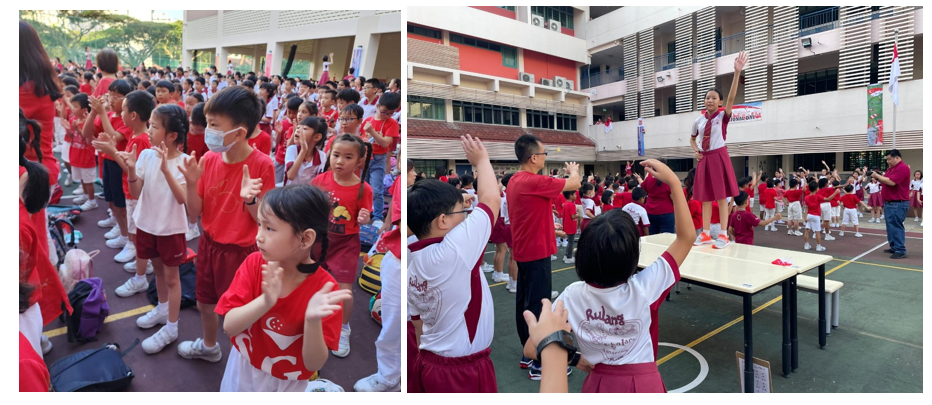 Students in red and white uniforms participate in a school outdoor event, with a girl leading from a table.