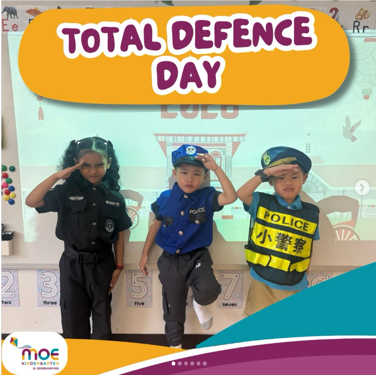 A "Total Defence Day" graphic from MOE Kindergarten @ Sembawang, showing three young children dressed in police and security uniforms, saluting and posing playfully in a classroom decorated with alphabet and number charts.