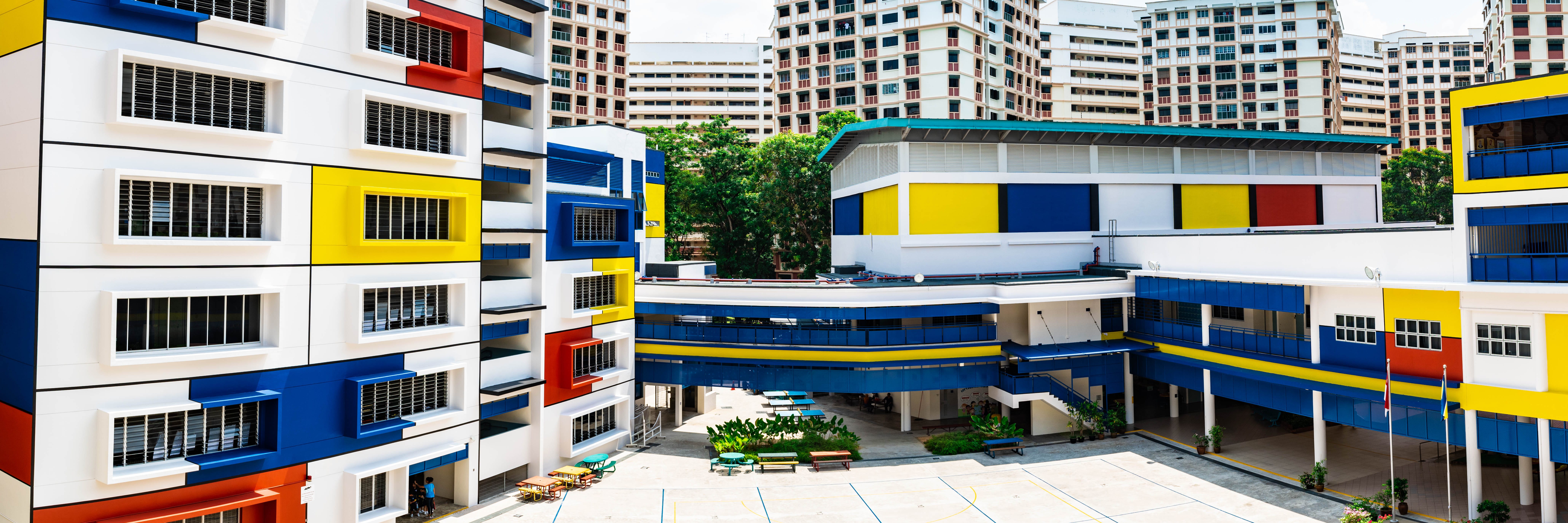 Colorful school courtyard with blue walkways, yellow panels, and tall apartment blocks in the background