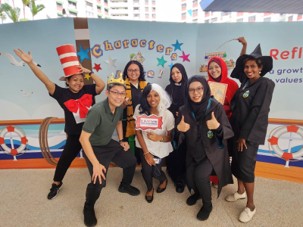 A group of teachers in colourful storybook costumes (including Cat in the Hat, a witch, and Hogwarts robes) pose cheerfully in front of a "Characters Alive" backdrop.