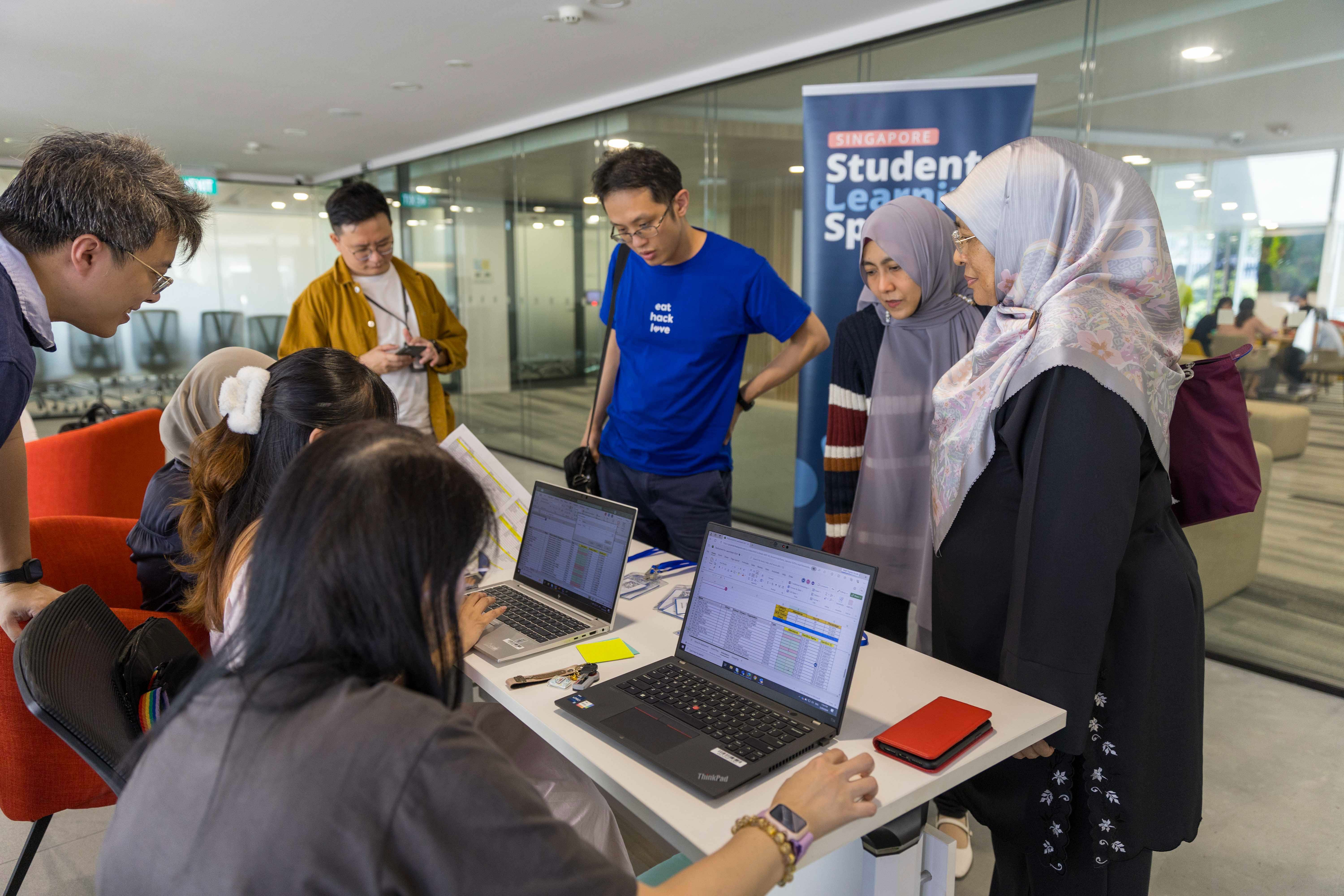 Several people gather around a registration table with two laptops at a Singapore Student Learning Space event.